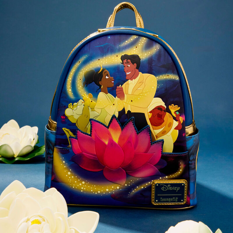 Dark blue Loungefly mini backpack featuring Princess Tiana and Prince Naveen dancing together surrounded by fireflies and other Princess and the Frog characters. There’s an applique water lily on the front. The bag sits against a blue background surrounded by white water lilies. 